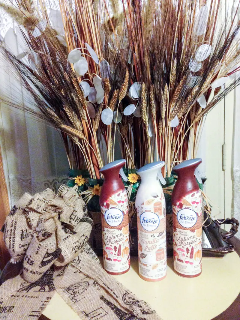 The three Febreze Air Effects Sprays set in front of a wheat floral display with a burlap bow off to the side.