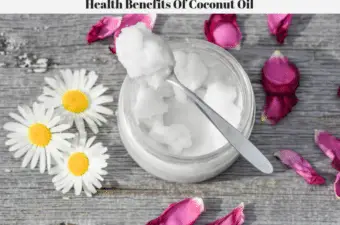 A jar of coconut oil with a spoonful laying on top of the jar. Daisies and rose petals are laying on the table around the edge of the jar of coconut oil.