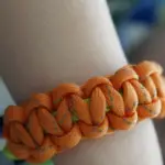 An orange paracord bracelet on a wrist.