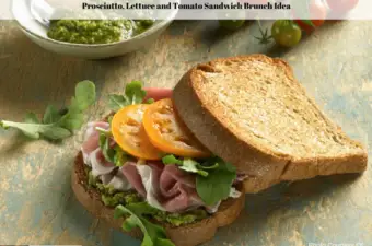 A prosciutto, lettuce and tomato sandwich on a plate with a bowl of pesto, fresh lettuce and whole tomatoes sitting off to the side.