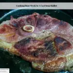 A ham steak cooking in a cast iron skillet.