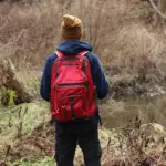 A person in the wilderness with a bug out backpack standing near a creek.