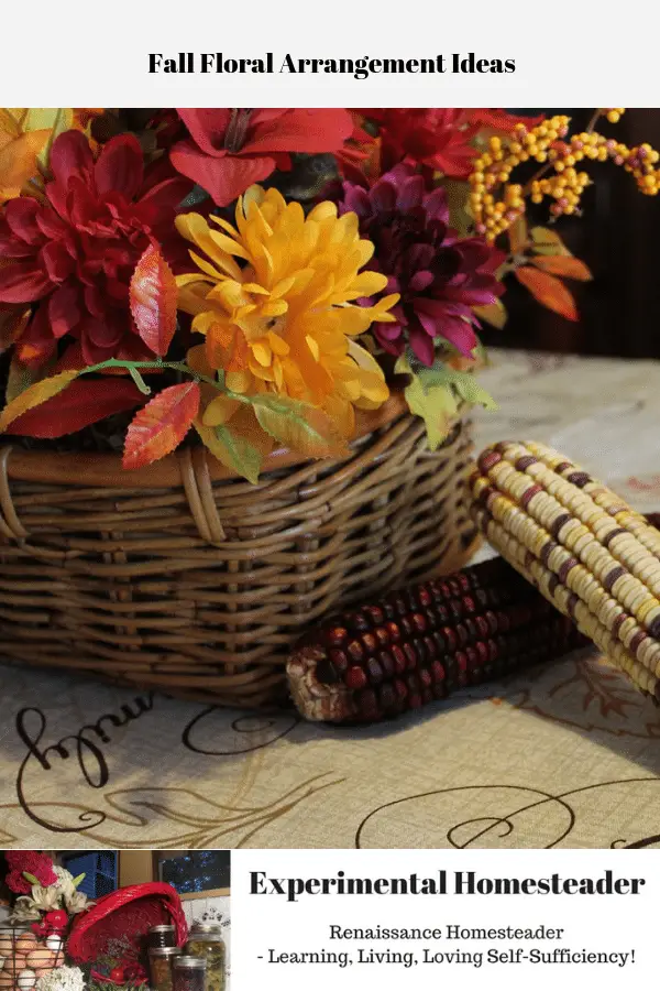 Fall flowers in a wicker basket, a couple ears of Indian corn and a mason jar with a lit candle inside all sitting on a table.