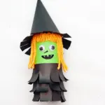 A witch made out of an empty toilet paper roll, yarn and construction paper.