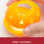 A hand putting the top of the orange on the bottom half of the orange that has a candle in it for a luminary decoration.