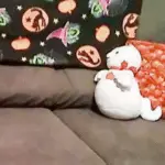 A plush ghost sitting on a couch in front of a pillow.