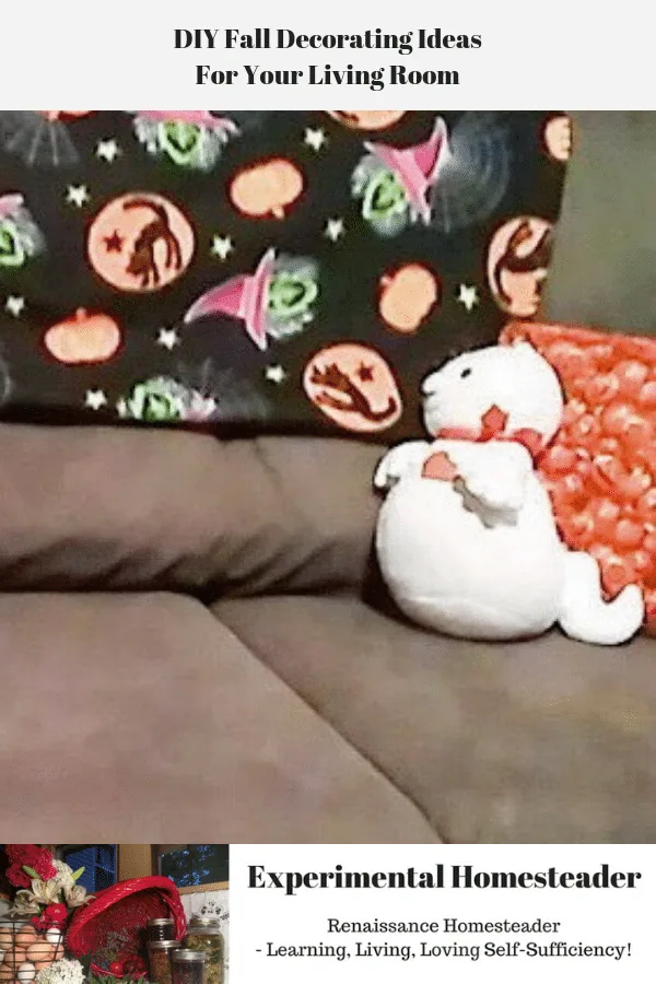 A plush ghost sitting on a couch in front of a pillow.
