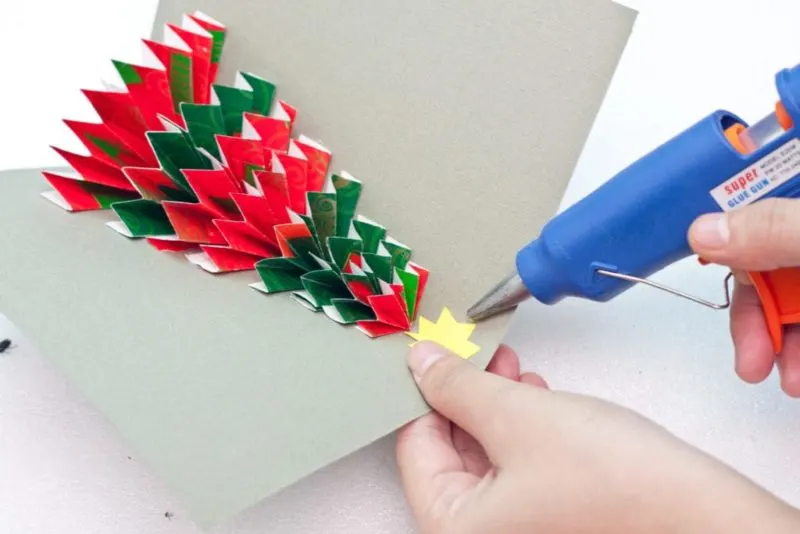 A yellow star being glued to the top of the tabletop Christmas tree card.
