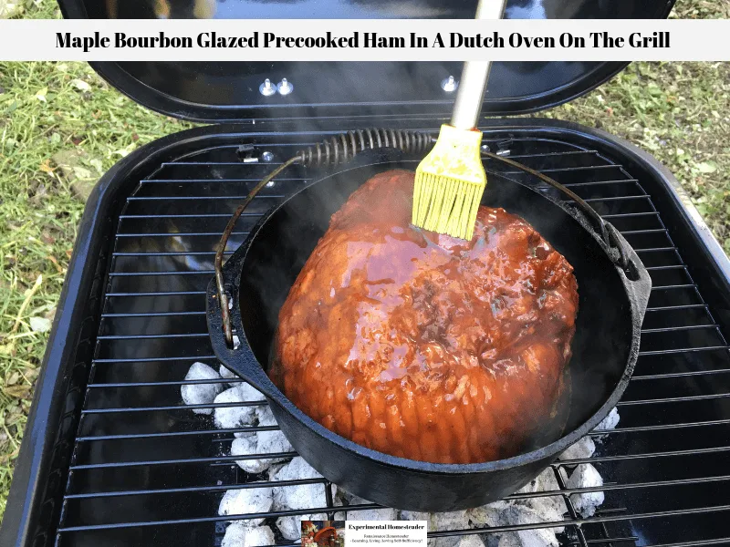 Frick's Super Trim Bone-In Ham With Natural Juices being glazed with a maple bourbon glaze and cooked in a cast iron Dutch Oven on a charcoal BBQ grill.