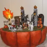 A Maker's Halloween Pumpkin Container decorated to look like a graveyard fairy garden complete with skeletons, skull animals and an LED lighted tree.