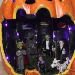 A ready to display Maker's Halloween Littles Jack O'Lantern Container Fairy Garden lit up with purple LED lights.