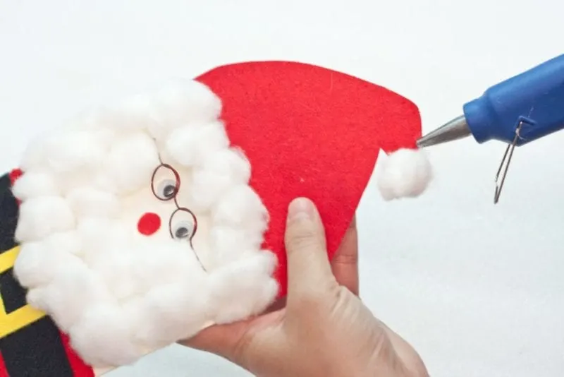 A cotton ball being glued on Santa's hat.