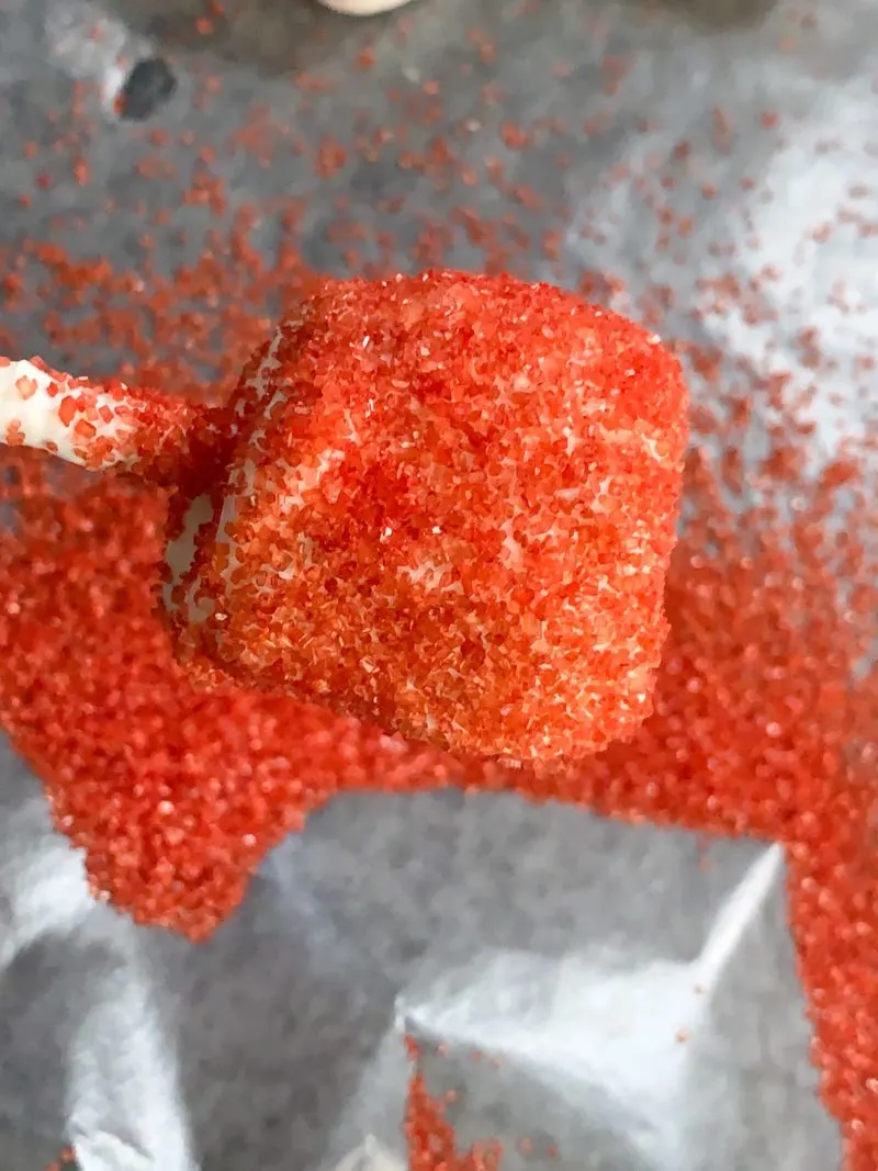 The chocolate covered marshmallow being covered in red sugar crystals.