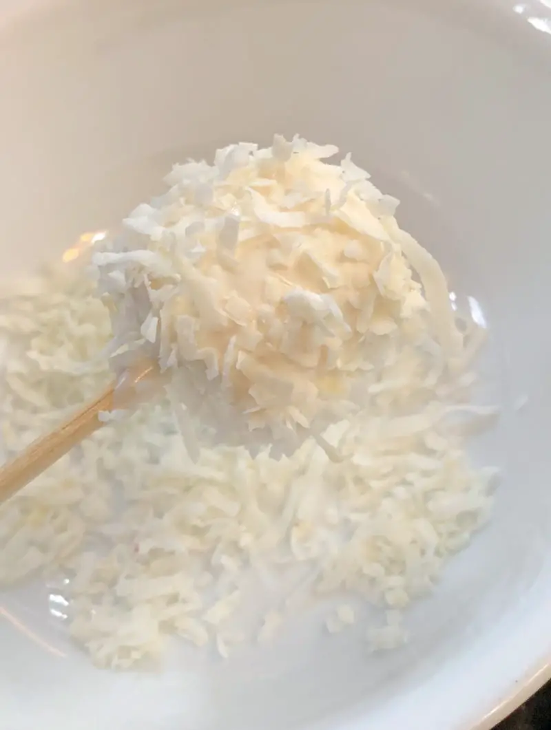 A marshmallow on a wooden skewer being coated in coconut flakes.