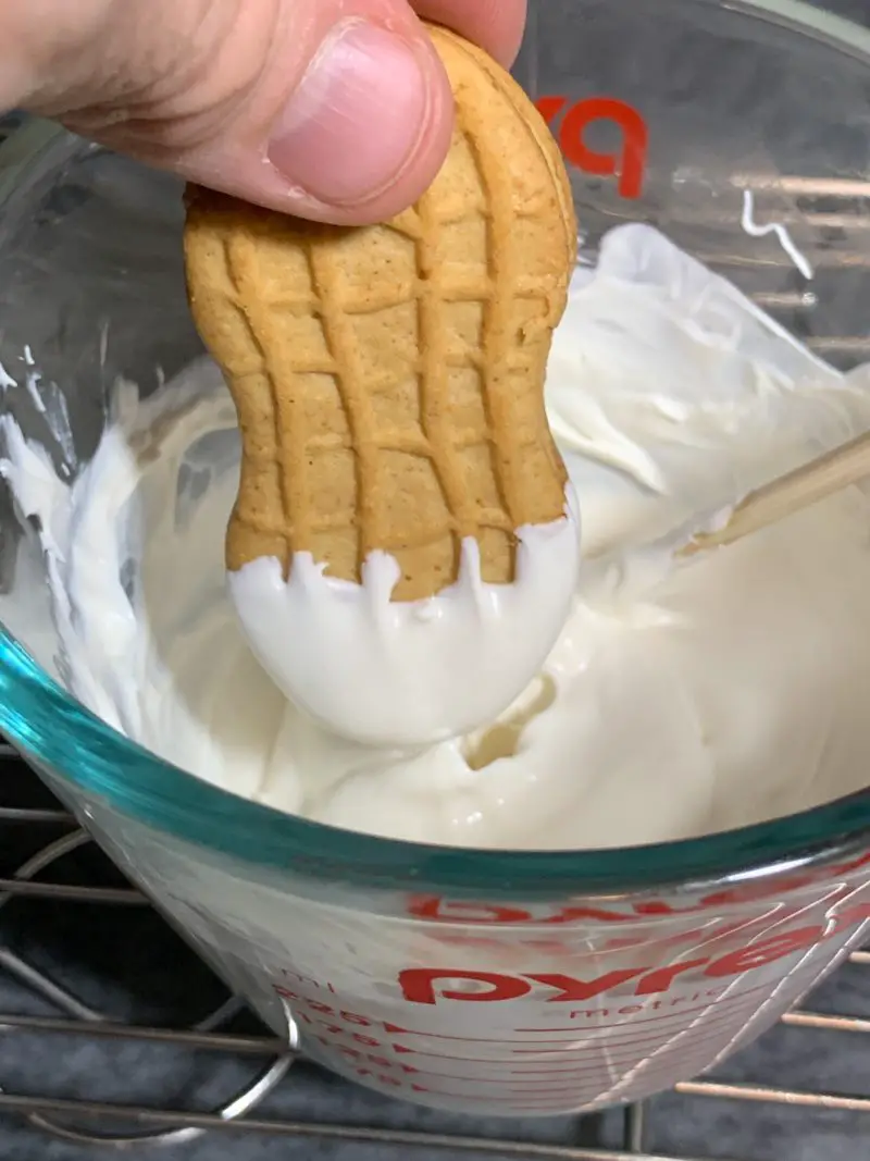 Dipping the Nutter Butter Sandwich cookie into the melted white chocolate.