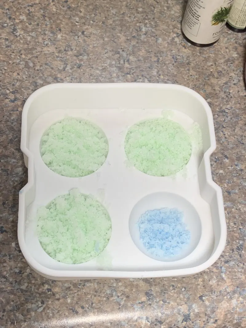 The green bath bomb mixture being placed on top of the blue bath bomb mixture in the mold.