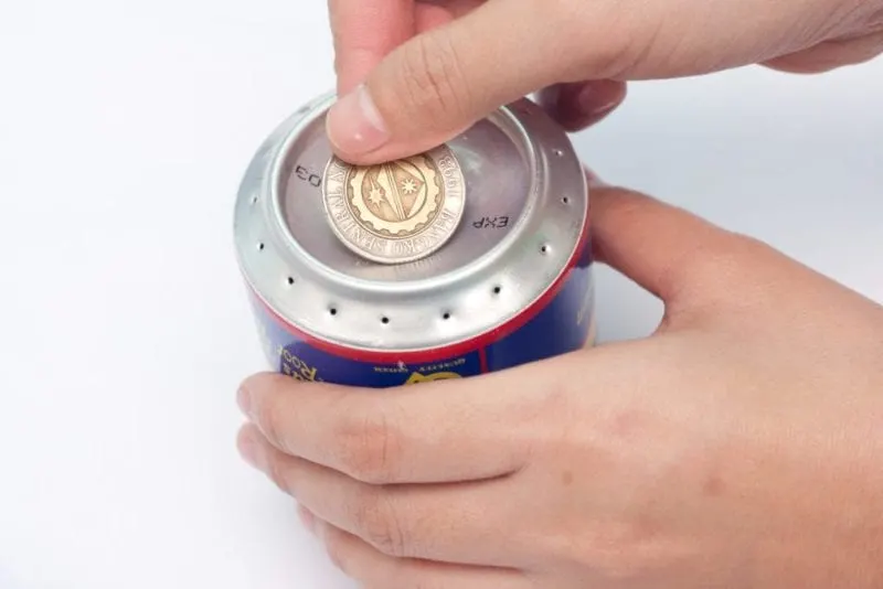 A coin being placed over the large hole in the center of the soda pop cans.