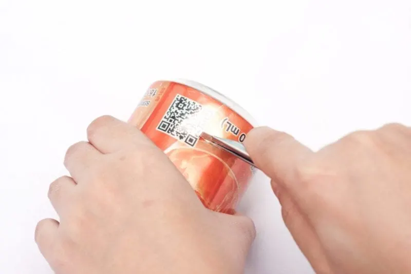 A sharp knife is being used to slice off the bottom of a soda can.