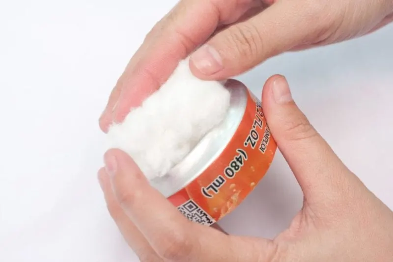 A large wad of cotton being placed on the bottom of one of the soda pop cans.
