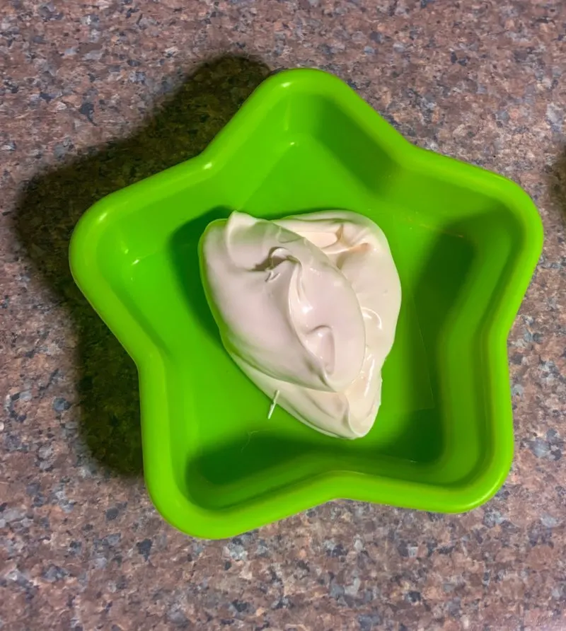 A spoonful of the white candy melts on top of the chocolate transfer mold.