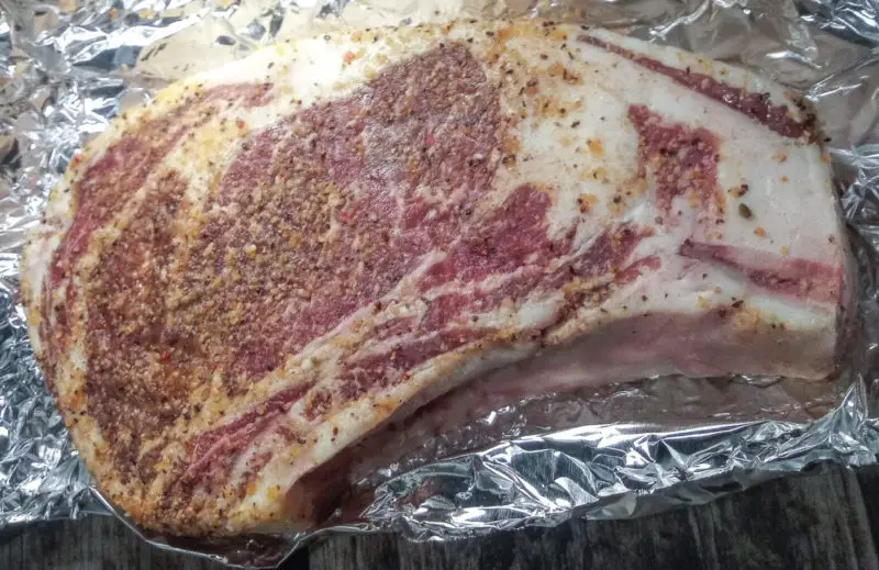 Uncooked ribeye steak on a piece of aluminum foil being seasoned.