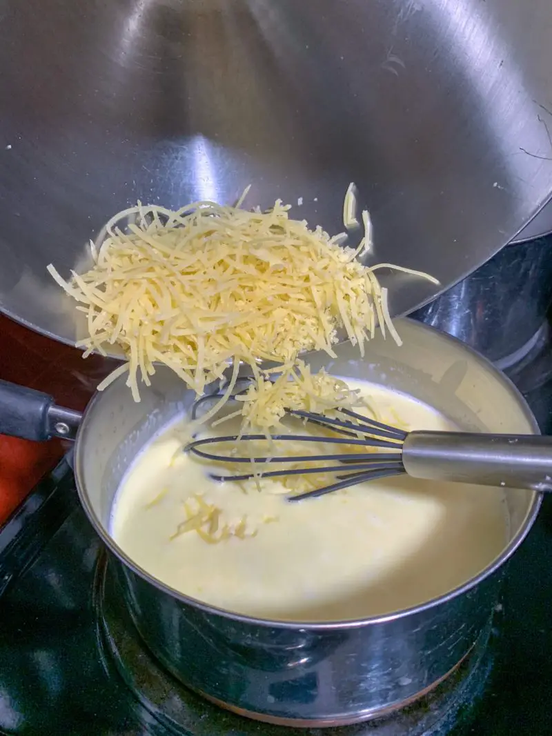 The cheese being poured into the creamy pasta sauce.