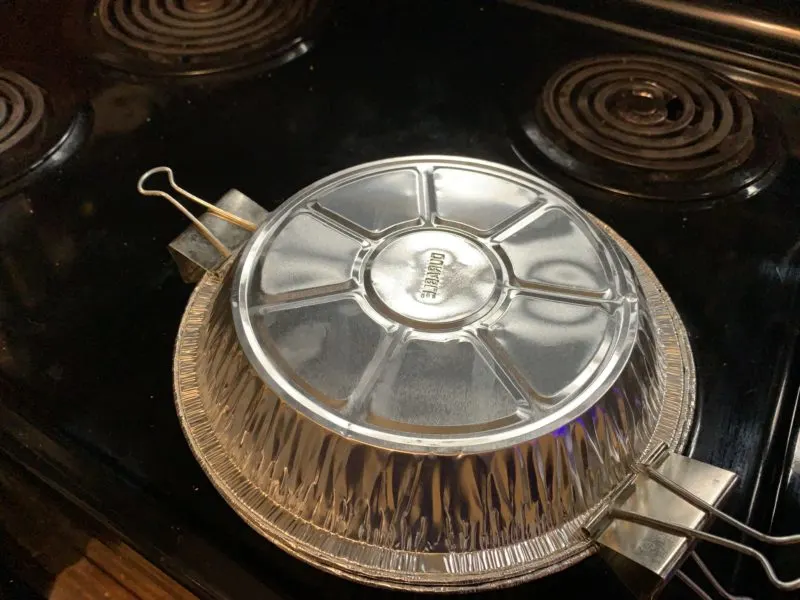A second pie pan placed on top of the first pipe pan and secured using paper clamps.