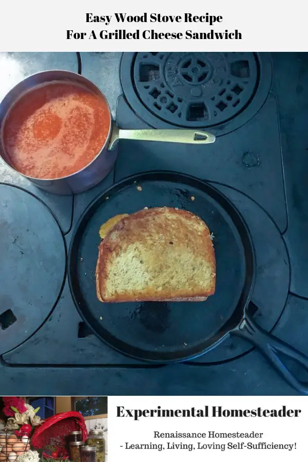 A grilled cheese sandwich cooking in a cast iron griddle on top of a wood burning stove with a pan of tomato soup on the side.