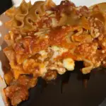 A slice of this cooked cheese lasagna being lifted out of the pan.