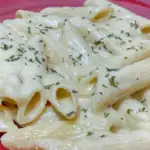 The creamy pasta sauce on the penne pasta on a plate, dusted with parsley and ready to eat.