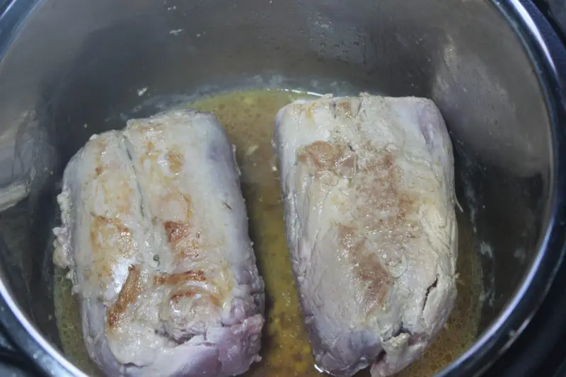 The pork tenderloin cut in half and being browned in the Instant Pot.