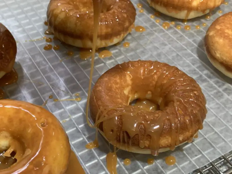 The caramel glaze being drizzled over the donuts.