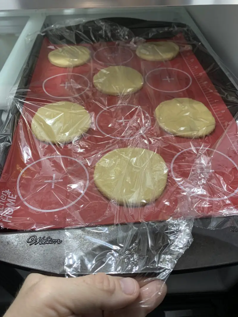 The covered sugar cookies being placed in the refrigerator.