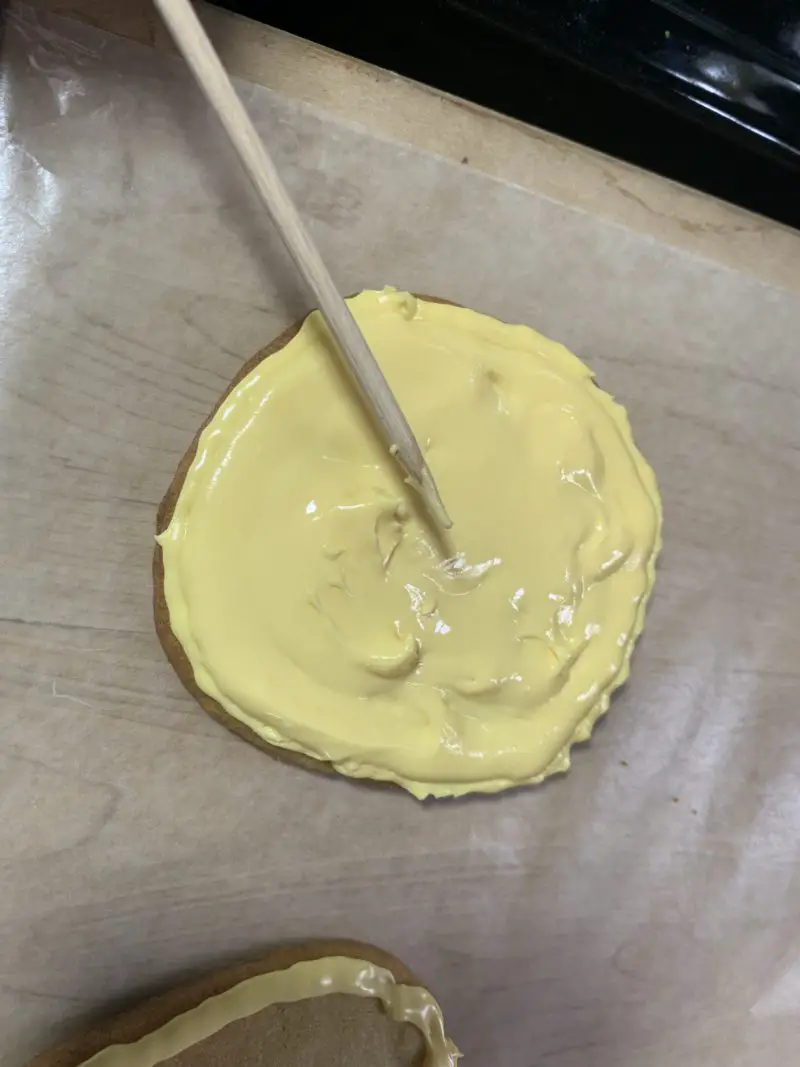 A wooden skewer being used to spread the icing on the cookie.