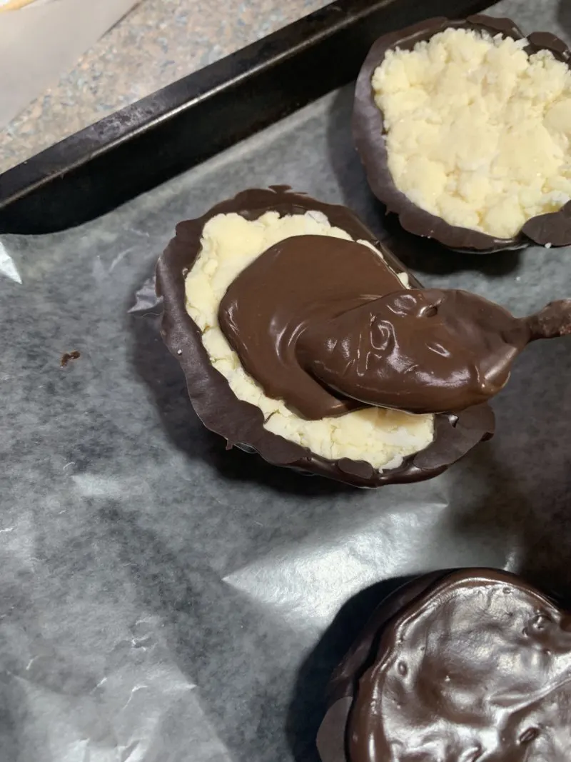 The dark cocoa being spooned on the bottom of the coconut creme filled eggs and spread around with a spoon.