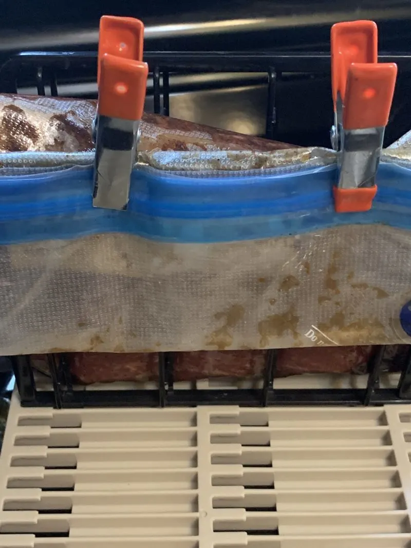 The sous vide bag containing the meat being secured to the rack.