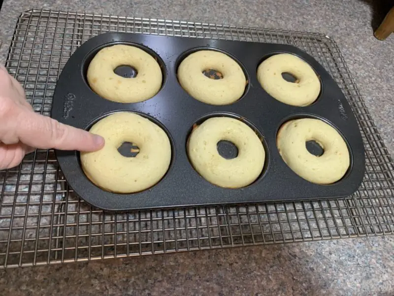 A finger touching the top of the donuts to make sure they are done.