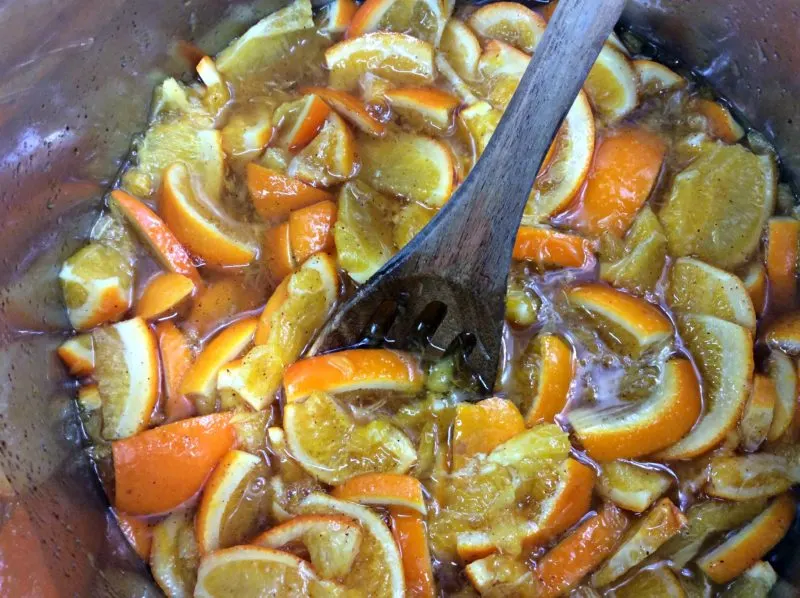 A wooden spoon being used to stir the clementine's in the Instant Pot.