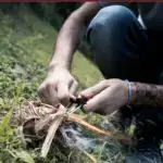 Someone starting a fire from scratch outdoors during a survival scenario.