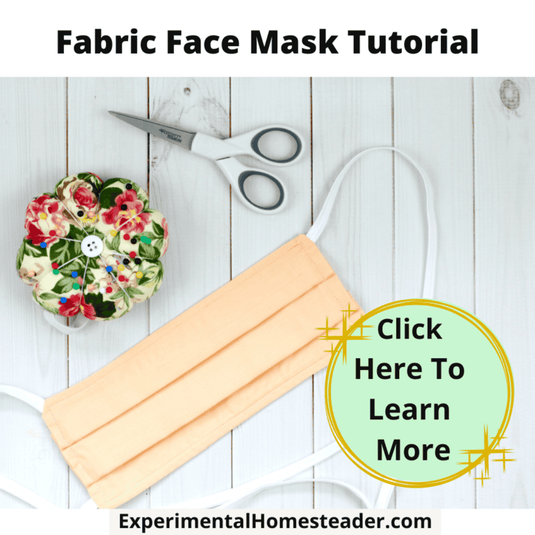Reusable fabric face mask with sewing and scissors on white wooden background.